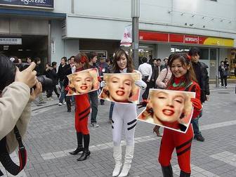 Photomontage in which three asian girls holding signs with your picture, in the street, with great anticipation.